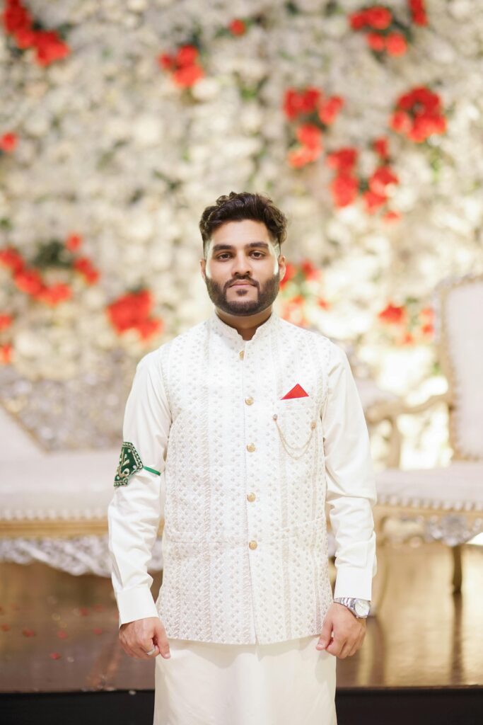 Portrait of a groom in traditional white attire with red and green accents at a wedding in Islamabad, Pakistan.